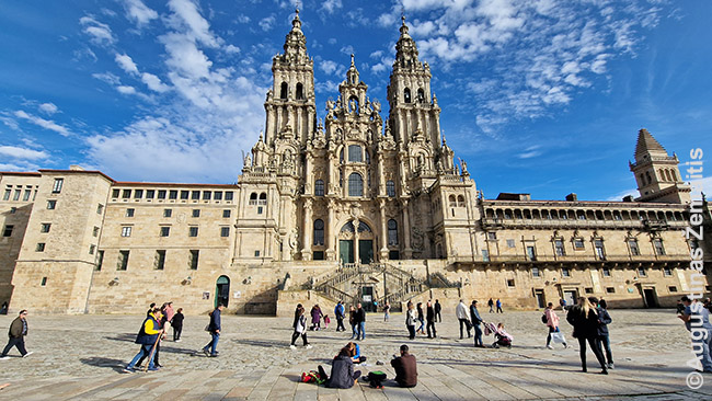 Ant žemės atsisėdę piligrimai gėrisi Santiago katedra