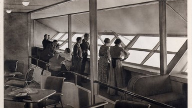 Dirižablio restorane keleiviai žiūri į apačią