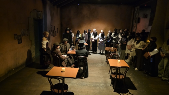 Žiūrovai (prie sienos) stebi sceną kavinėje, atsekę čia susitikti atėjusius herojus