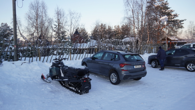 Sniegomobilis ir automobiliai tame pat parkinge